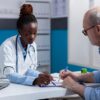 A doctor reviews paperwork with a senior male patient in an office. Photo: DC Studio / Freepik